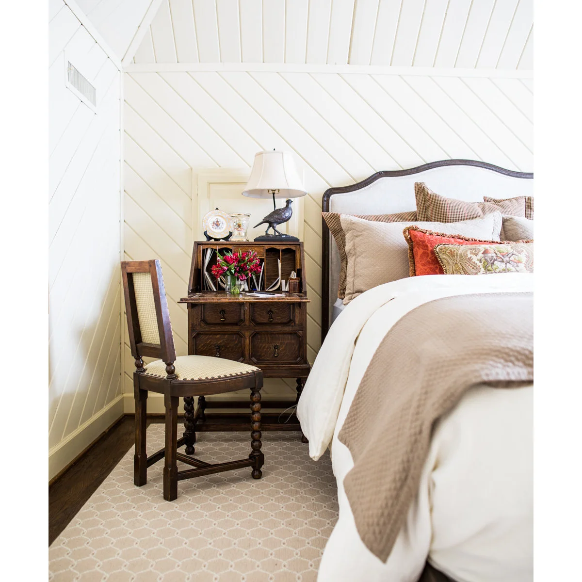 Small wood-colored secretary and cane-backed chair beside a pale upholstered bed