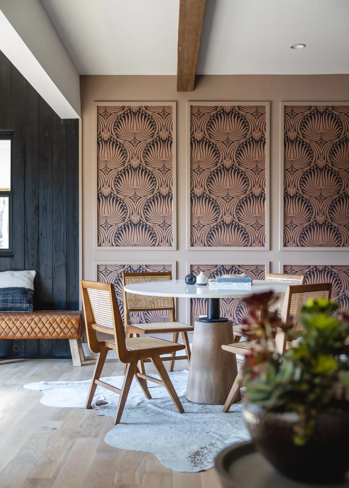 Cane chairs and a round table sit beside framed patterned wall panels.