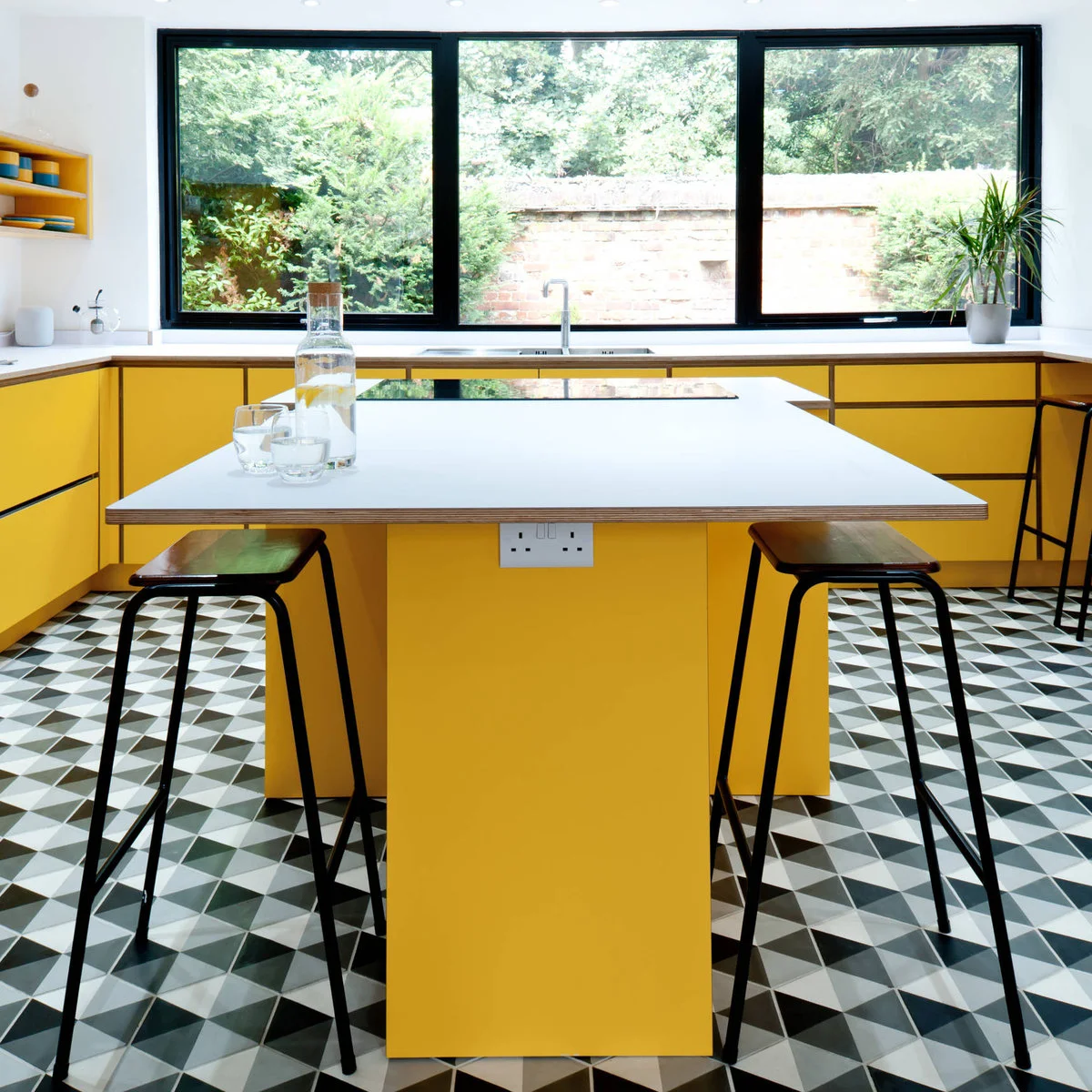 Bright yellow kitchen cabinets and island beneath black-framed windows with a geometric floor
