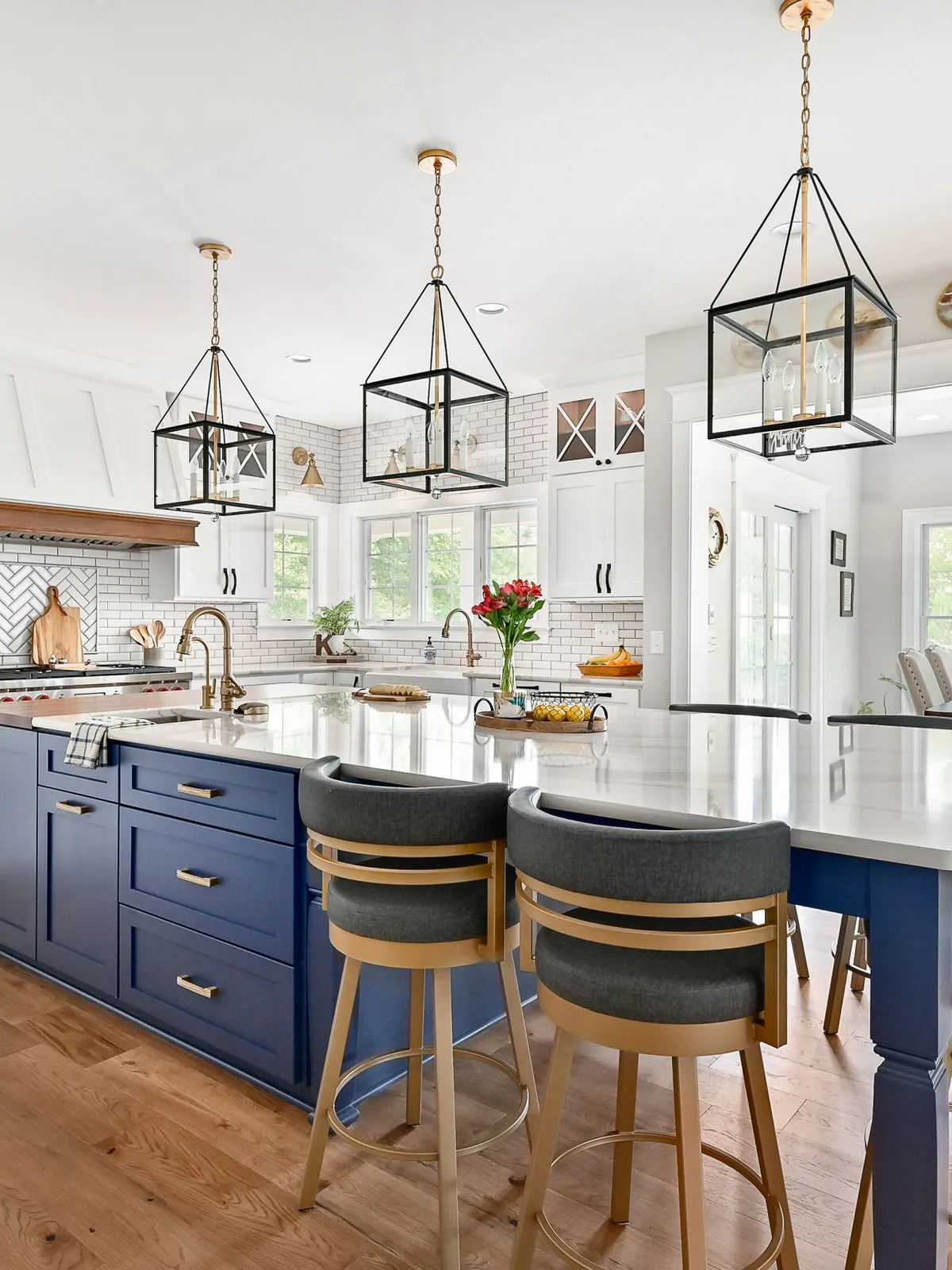 A navy island stands beneath open metal pendants with dark upholstered stools.