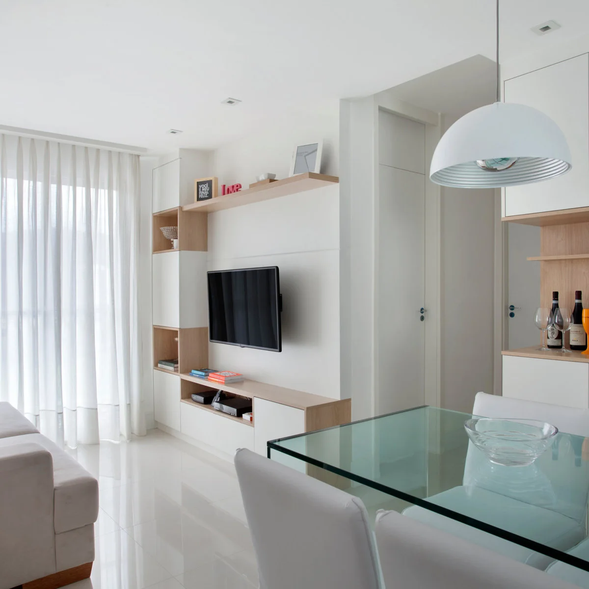 White media wall with pale wood shelves and cabinets beside a compact dining table