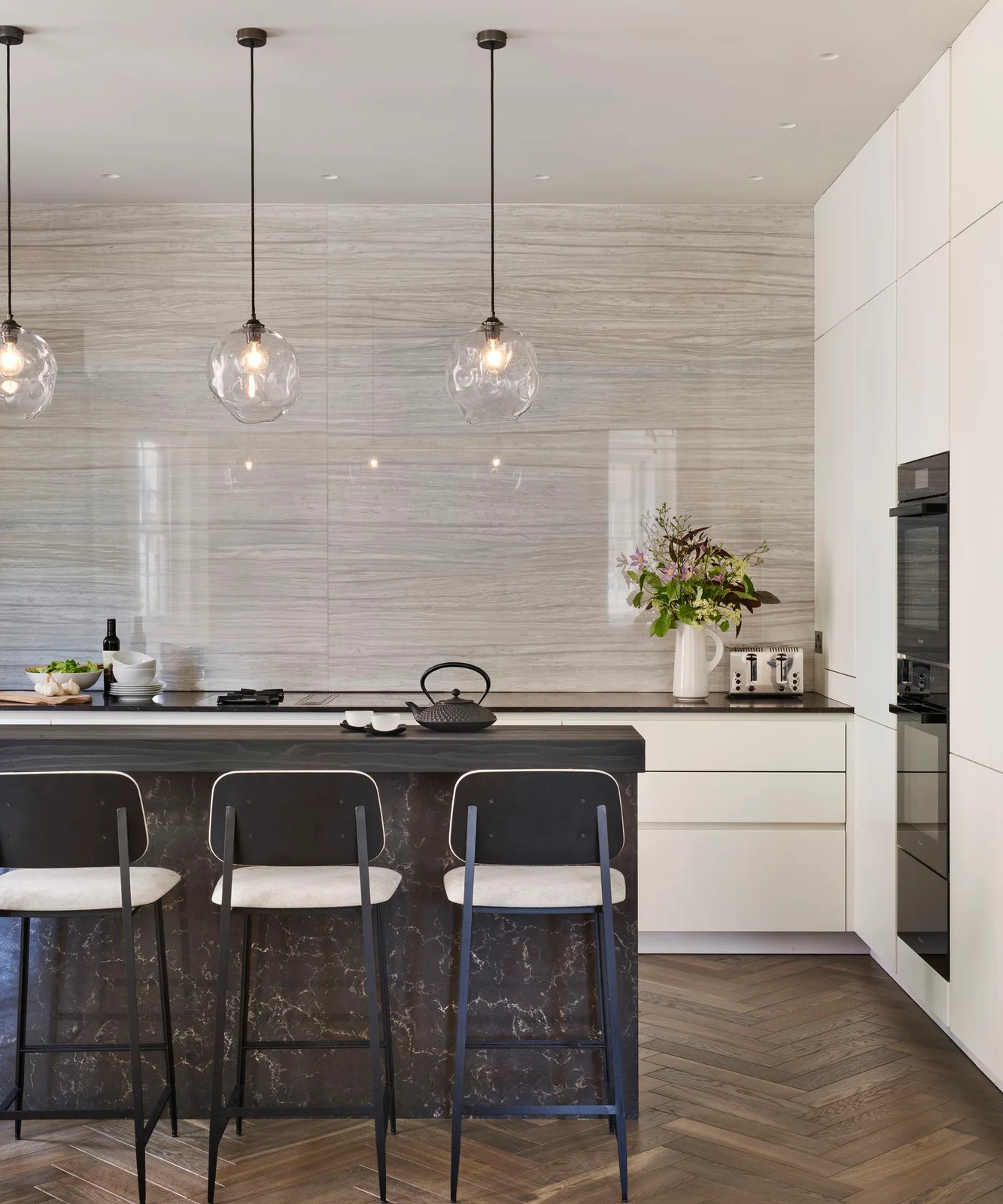 Plain soft-white tall cabinets and drawers sit beside a broad pale patterned backsplash and dark island.