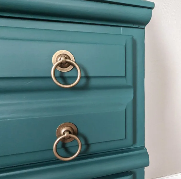 Close view of blue-green secretary drawers with round gold-toned ring handles and molded edges.