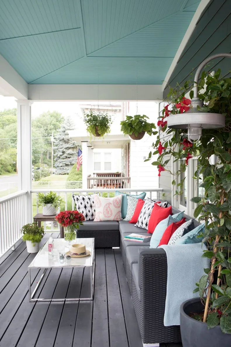 Gray porch sectional with red, pink and blue cushions beneath pale blue ceiling and hanging plants