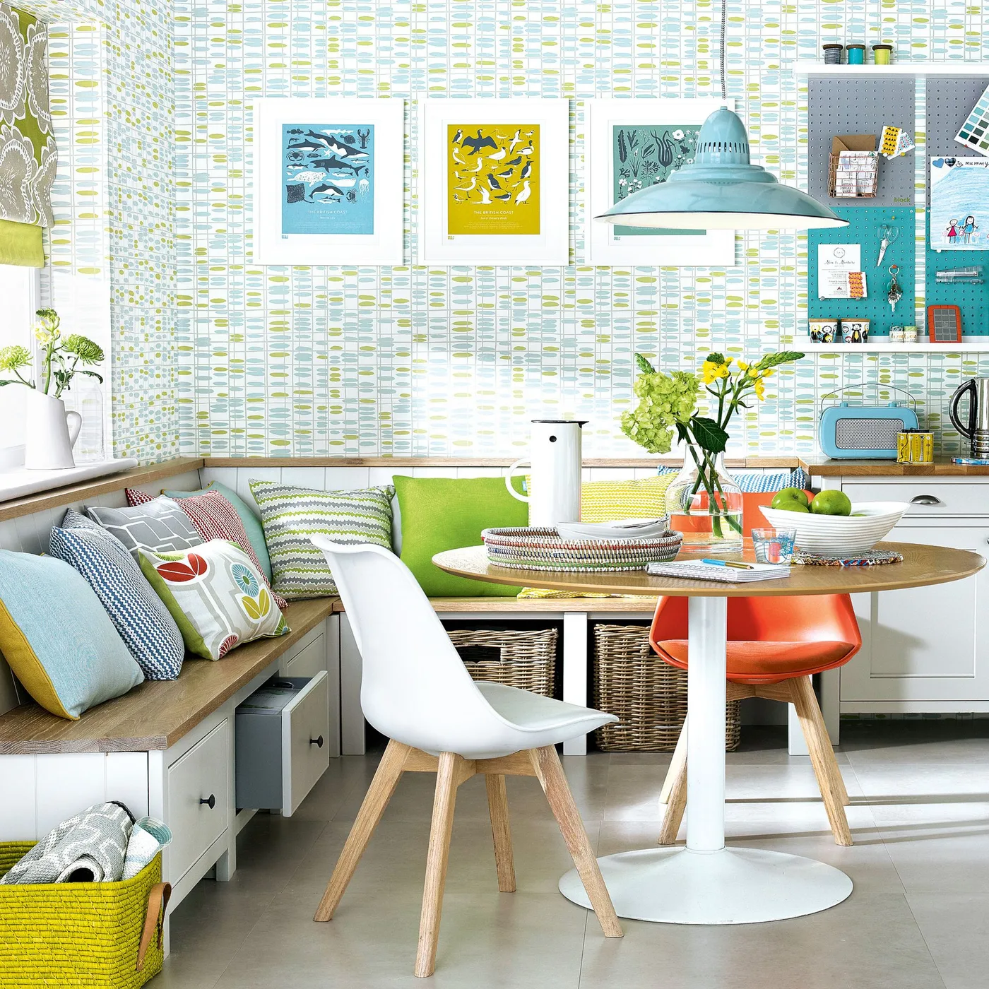 Colorful dining nook with a corner storage bench, green and gray cushions, round wooden pedestal table and mixed chairs.