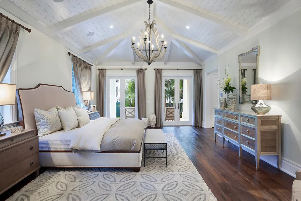 Reddish dark boards run beneath a pale bed and light curtains in a bright bedroom