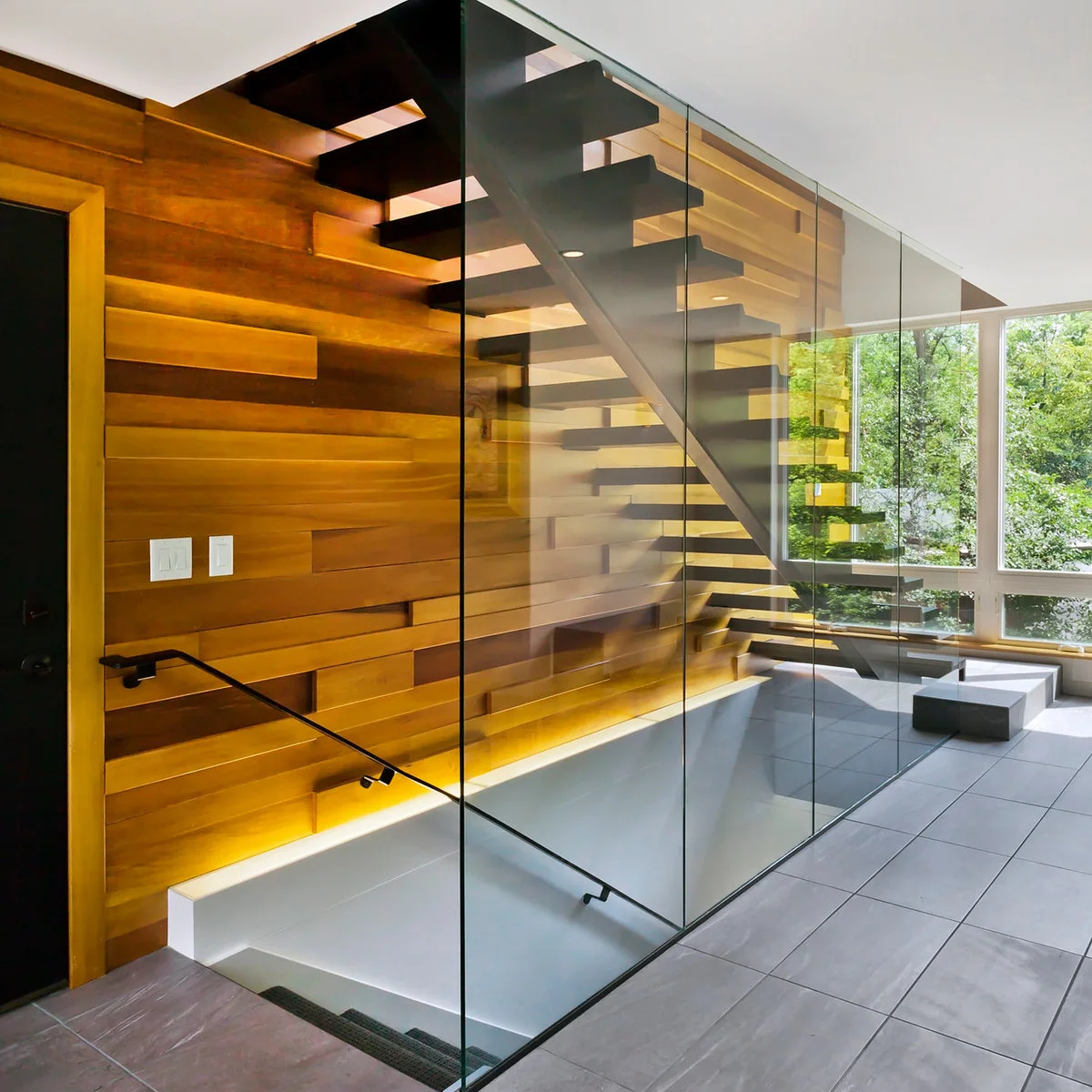 Warm light washes the lower part of a wood-clad stairway wall beside a dark open stair.
