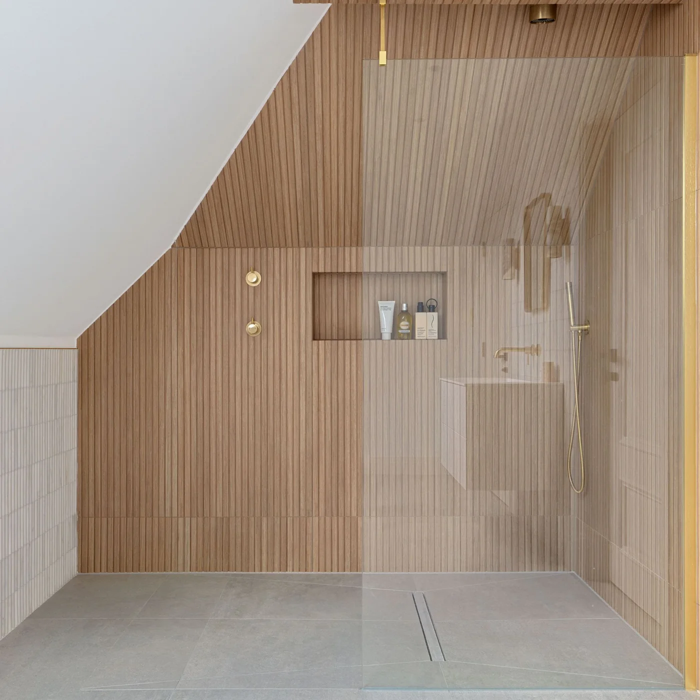 Warm reeded wood-effect tiles continue around a shower niche and sloped ceiling above a pale floor.
