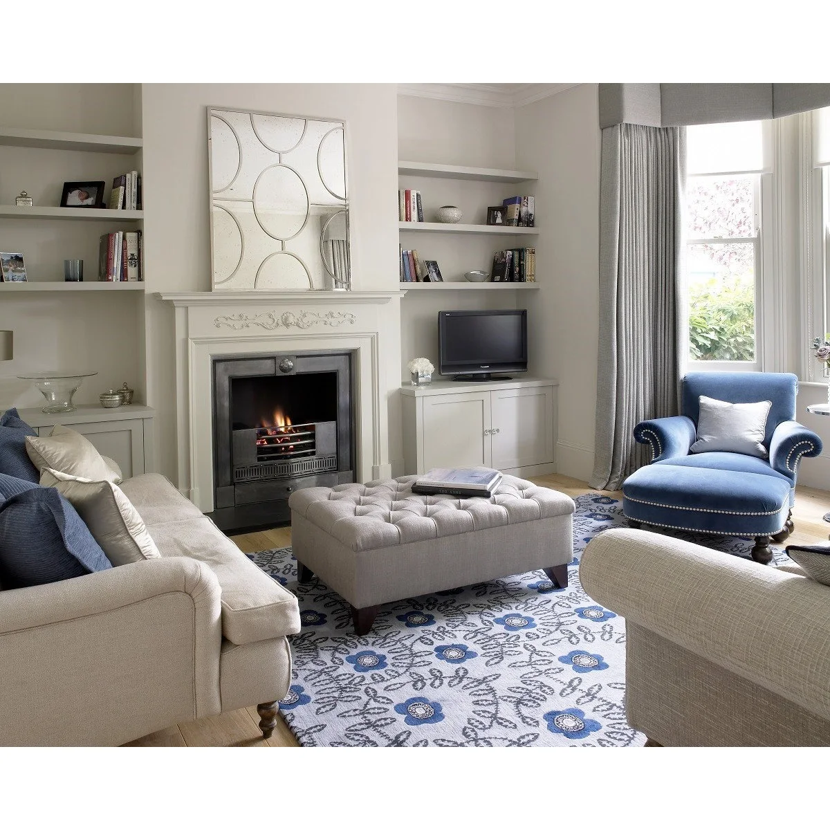 Two floating shelves with framed pictures, bowls and books above a small television in a white alcove beside a fireplace.