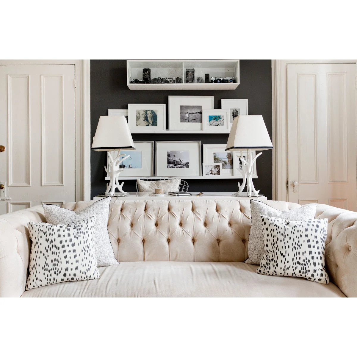 Pale tufted sofa with black-and-white cushions below pictures on a dark wall section