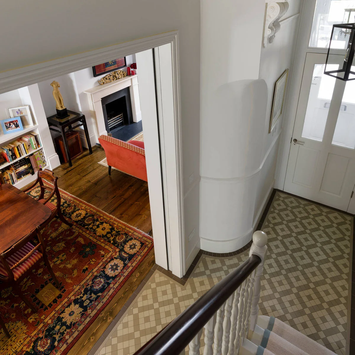 Compact tiled entrance seen from the stairs, with pale walls, a glazed front door and a wide opening into a living room.