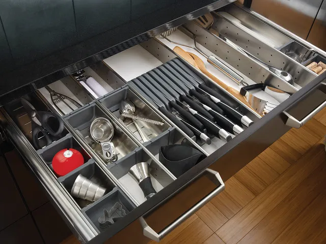 An open drawer beside dark cabinetry contains divided sections for utensils and knives.