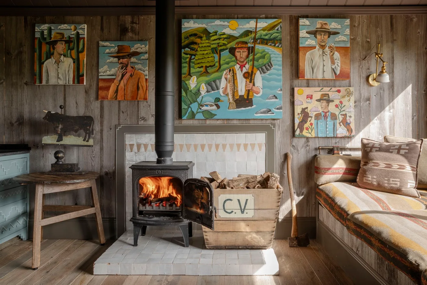 A black stove stands on a pale square tiled hearth in a wood-paneled room, with a patterned tile border behind and a log box nearby.