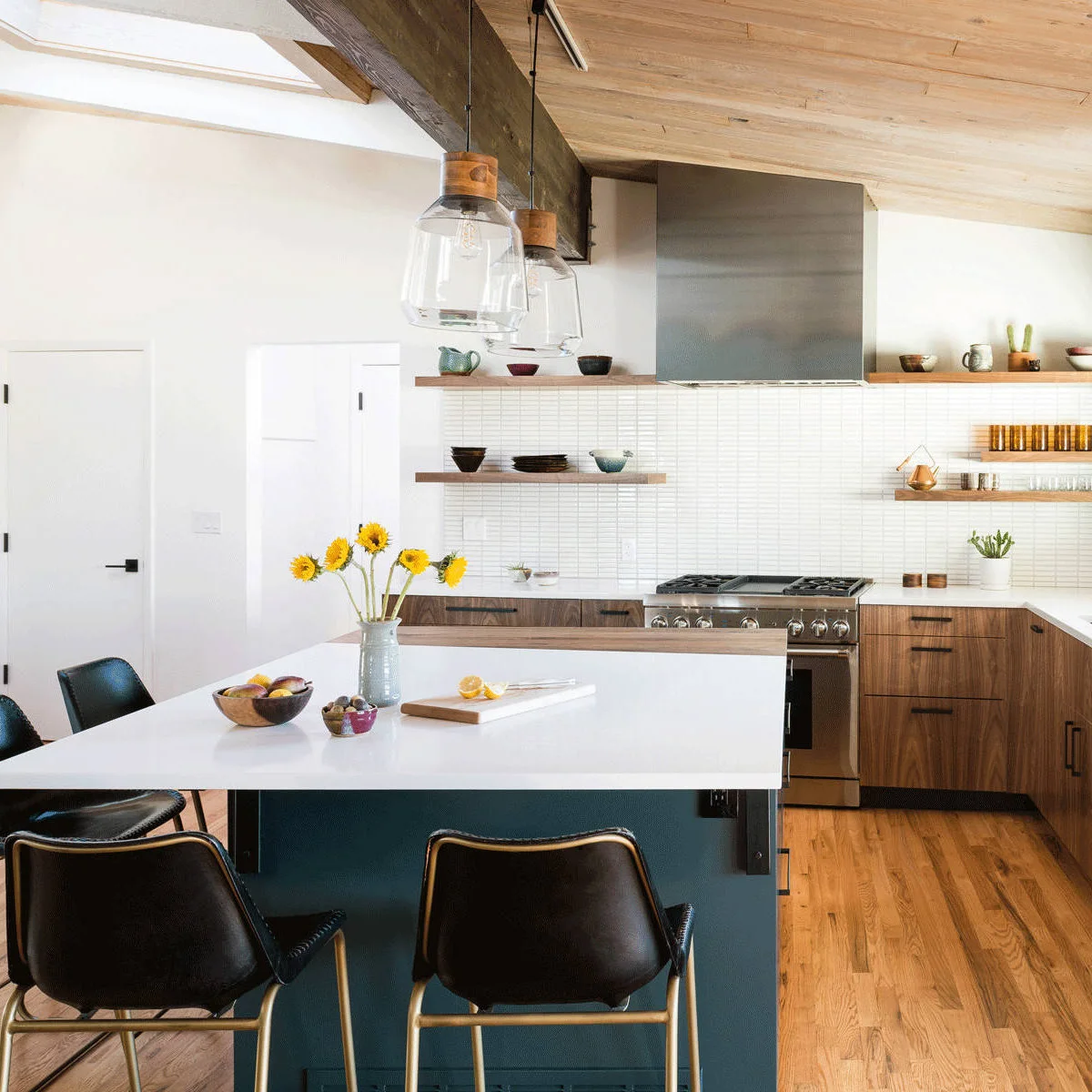Wood lower cabinets and a blue island beneath a wood ceiling and skylight, with pale walls and open shelves.