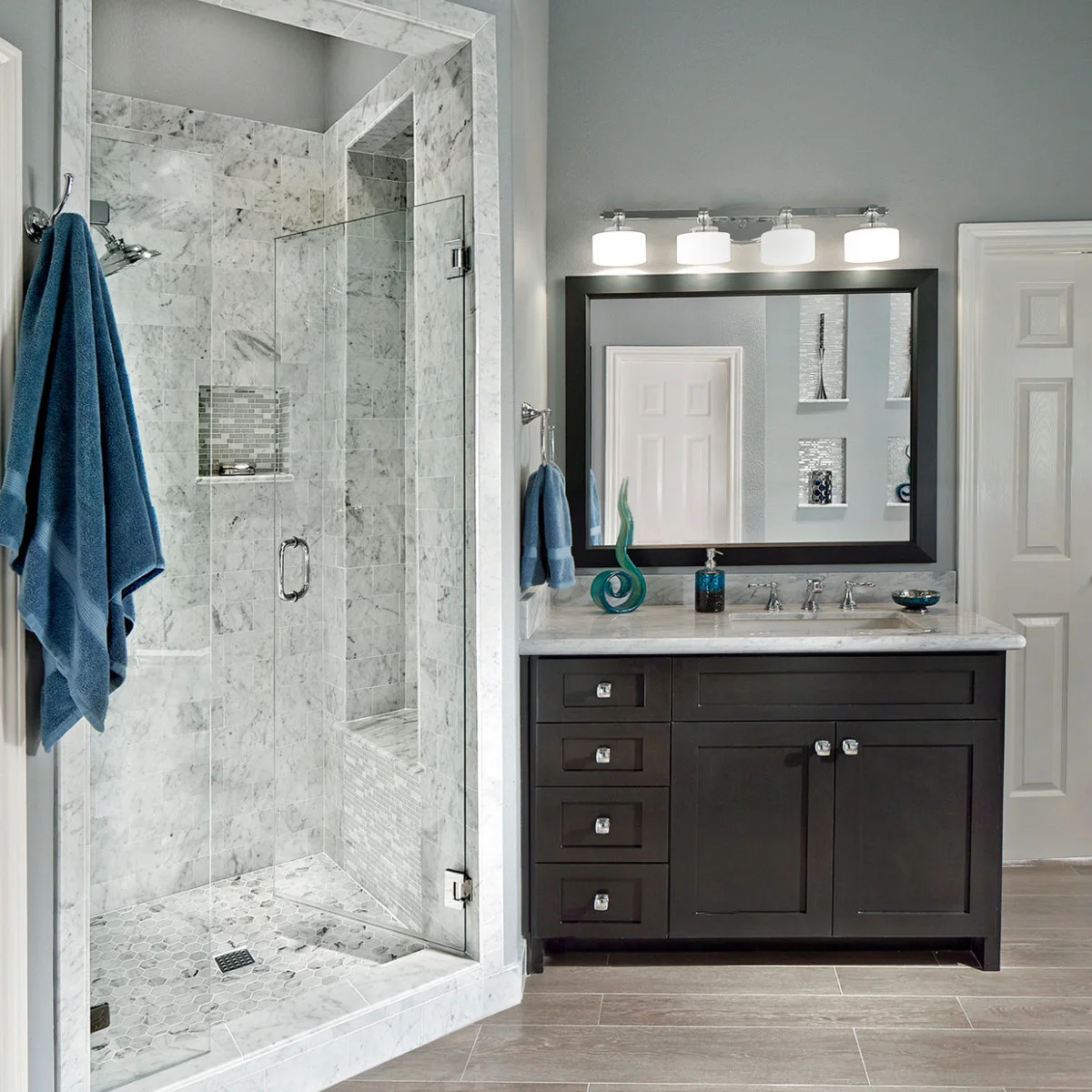 Pale veined shower walls and bench behind clear glass beside a dark vanity