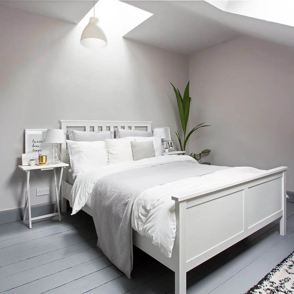 White bed and bedside tables in a pale gray attic room with roof windows and gray painted floorboards.