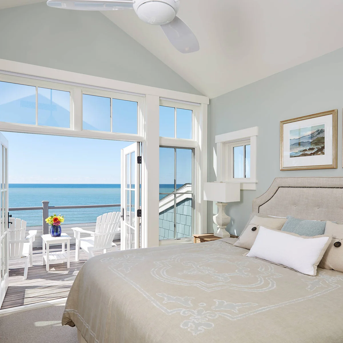 Pale blue-gray bedroom walls beneath a white vaulted ceiling with a cream bed and glazed doors.