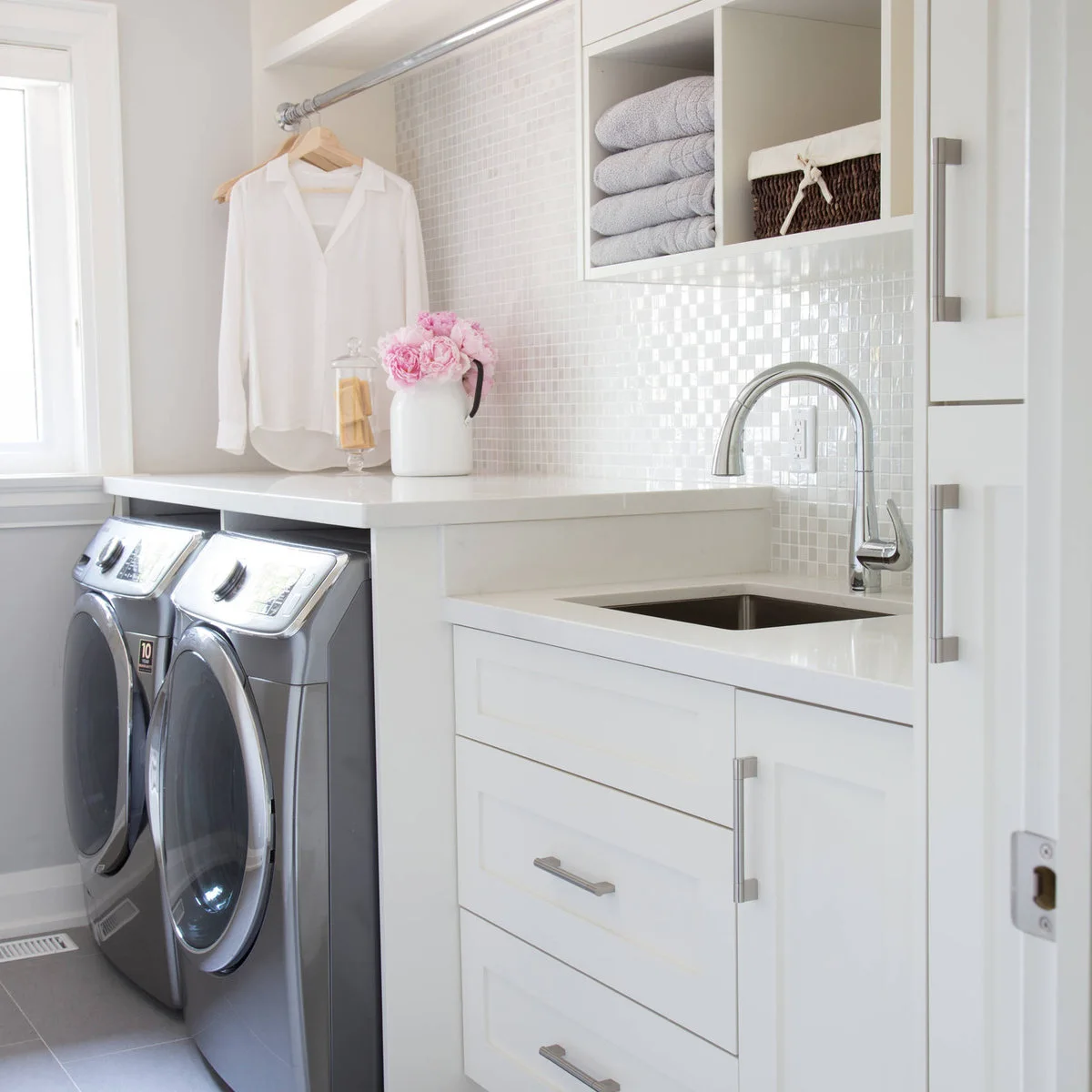 White laundry cabinets with a higher counter over silver appliances and a lower sink counter on the right