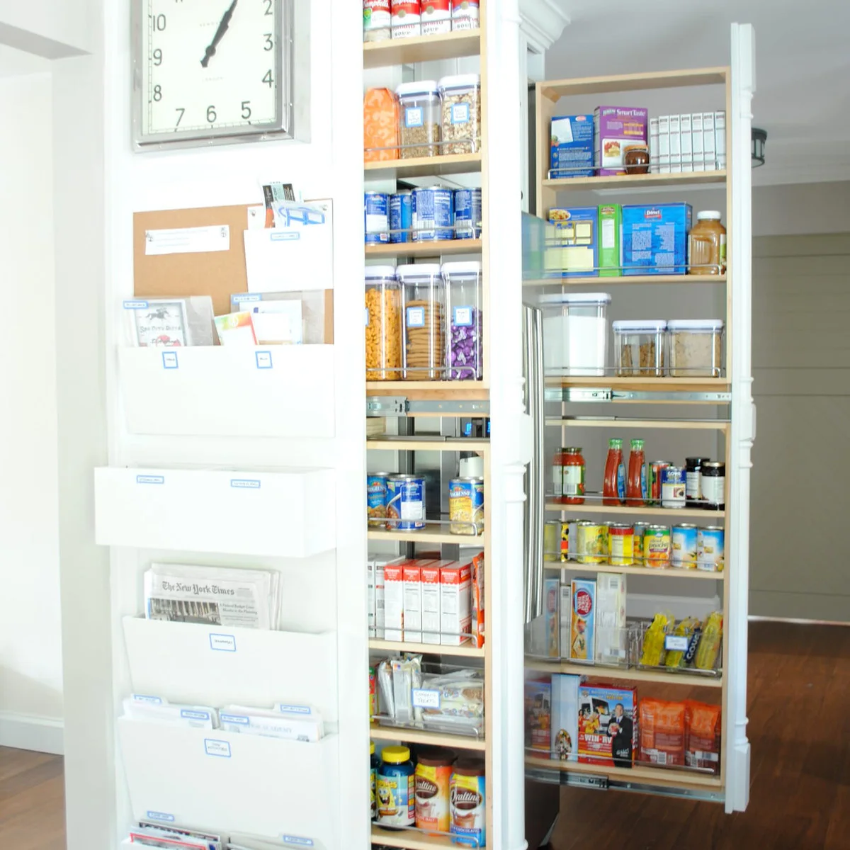Tall pull-out pantry beside wall-mounted paper pockets and a clock