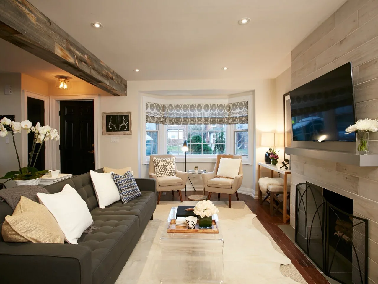 A charcoal sofa faces a pale coffee table and fireplace, with two cream chairs beneath a bay window.