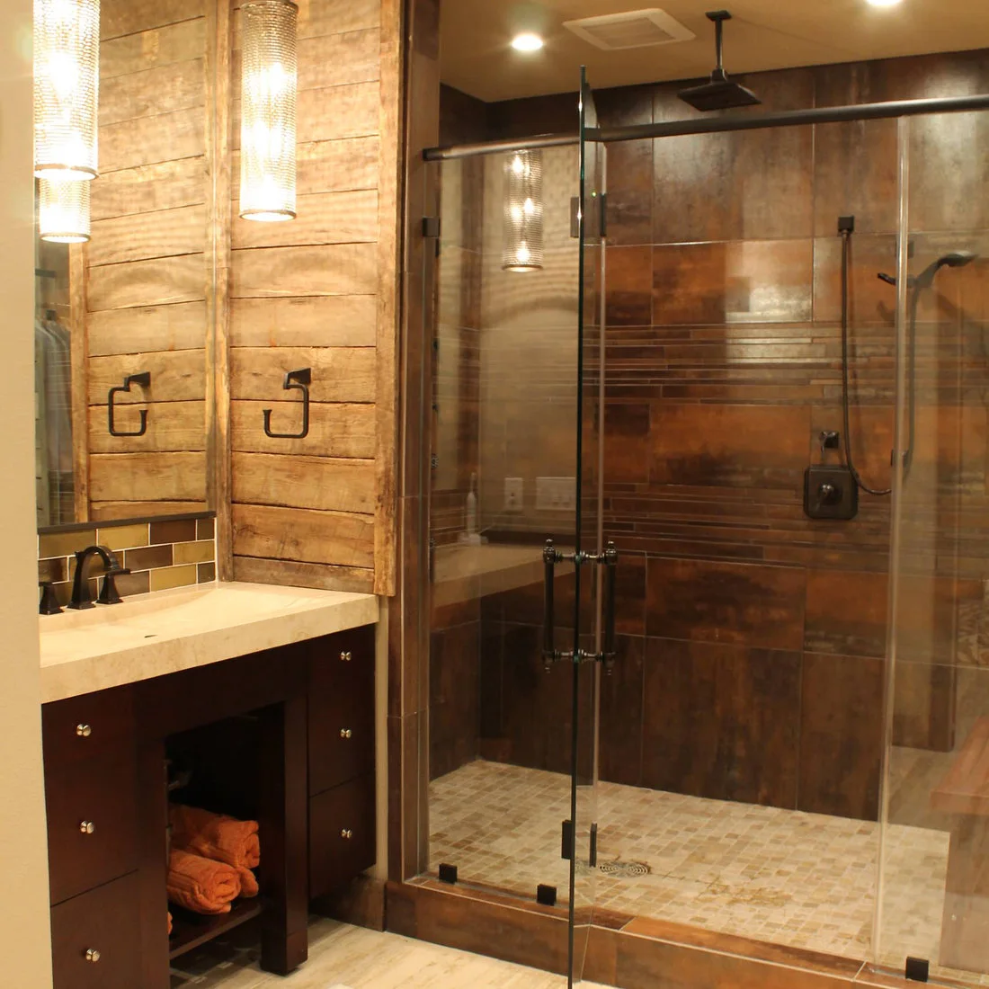 A glass shower with brown rectangular wall tiles beside a timber paneled basin wall