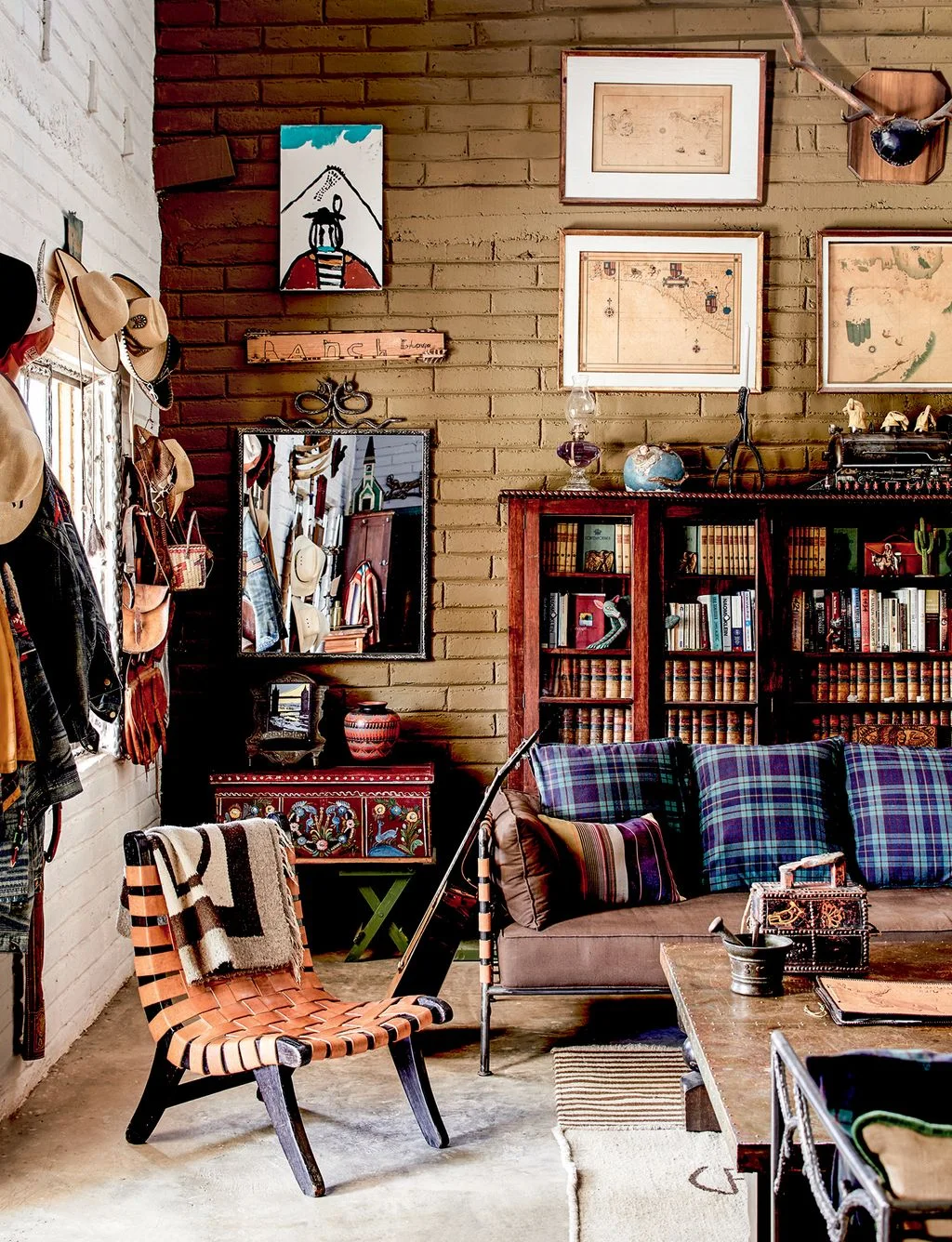 Collected sitting room with blue checked cushions, framed maps, dark book storage and a woven leather chair