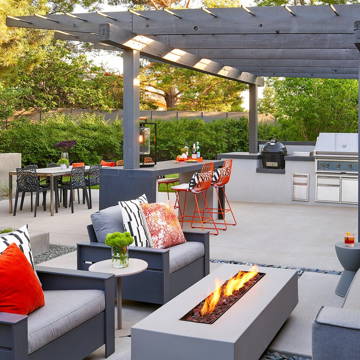 Gray backyard bar beneath a pergola with orange stools and matching orange cushions in the nearby lounge