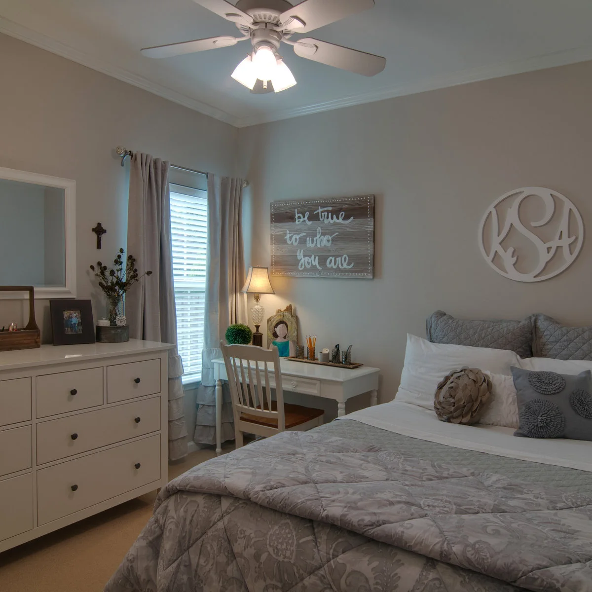 Gray teen bedroom with a small white desk beside a window and matching drawer storage