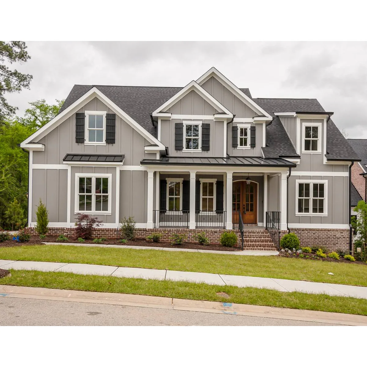 A gray house with a broad front porch, young rounded shrubs beside the steps and a narrow mulched planting bed.