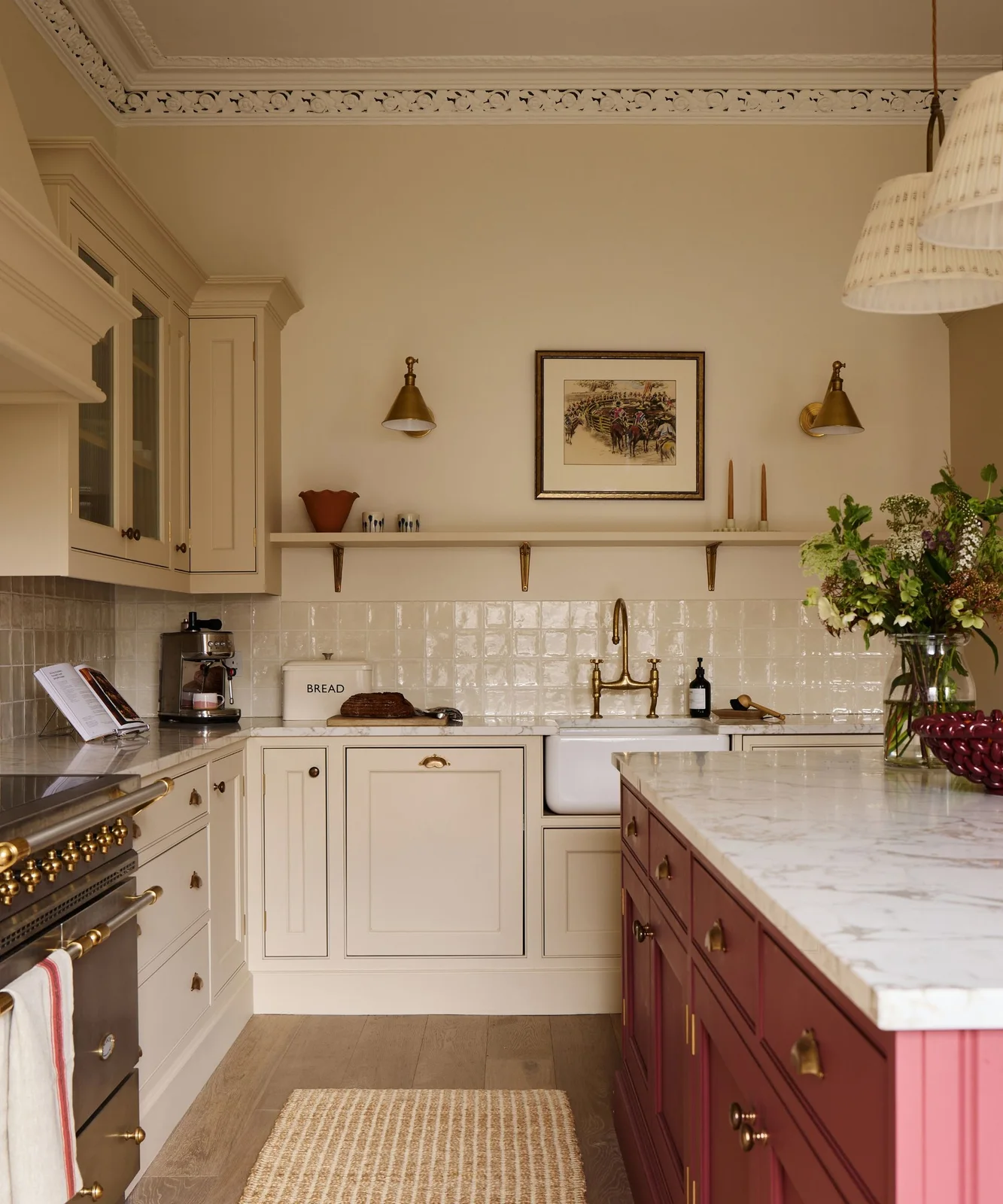Warm white framed cabinets with fine dark outlines sit beside a deep red island, brass-colored hardware and a broad sink.