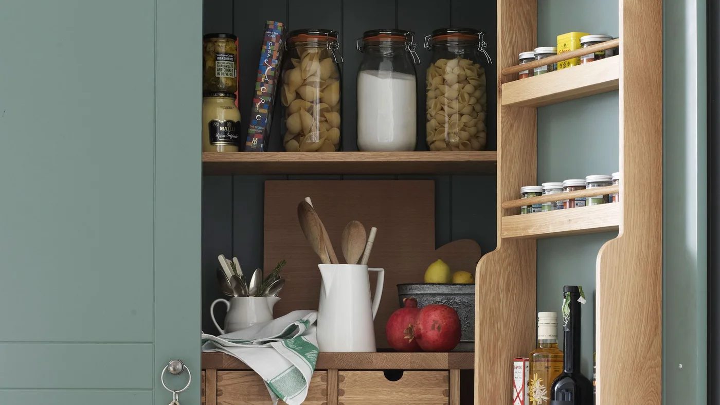 Green cupboard with utensils, cutting boards, clear jars and door-mounted spice racks