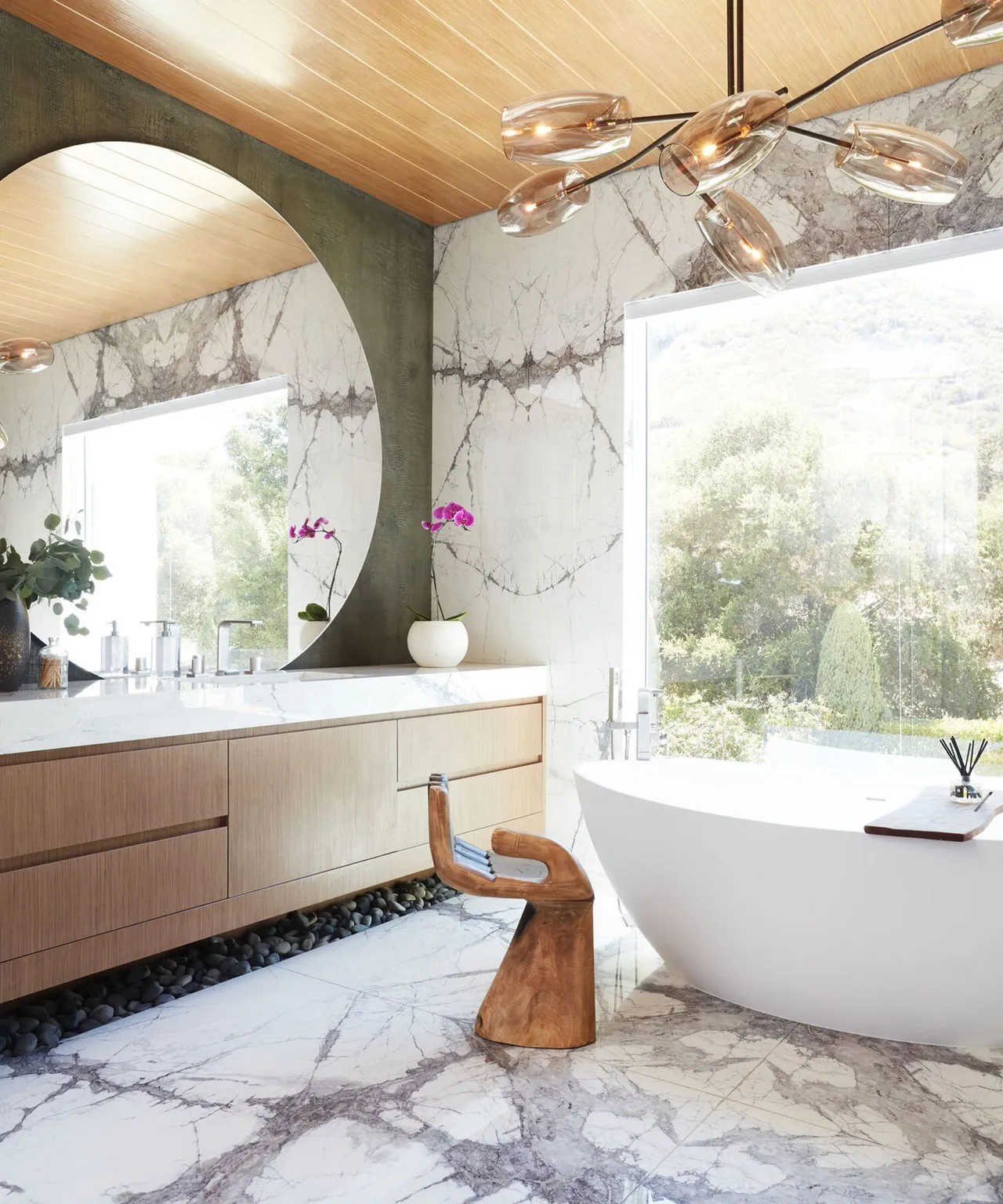 A timber-paneled ceiling spans a pale bathroom with broad windows and a simple bath.