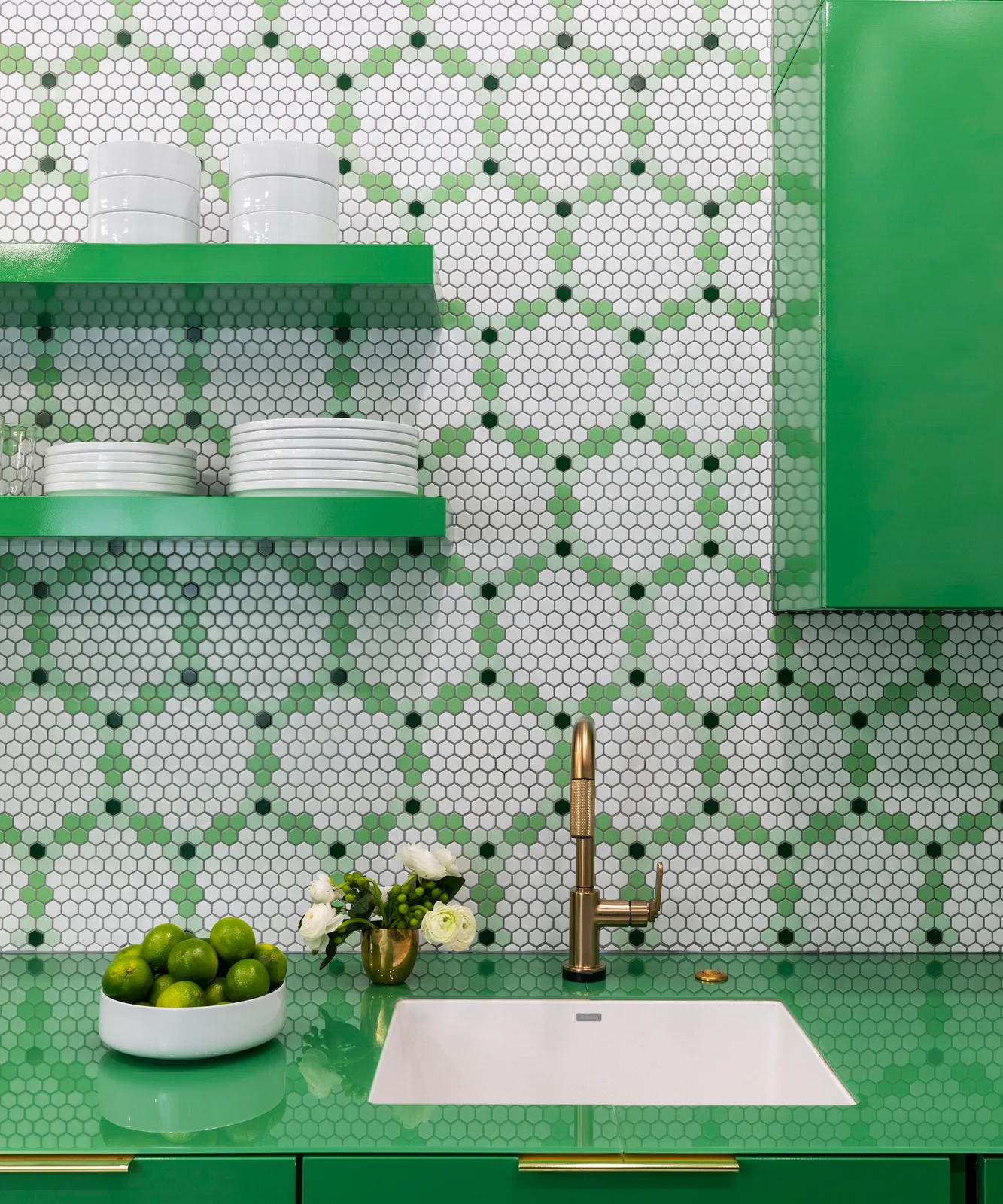 Small pale hexagonal wall tiles contain repeating green motifs above a bright green counter and sink beneath green shelves