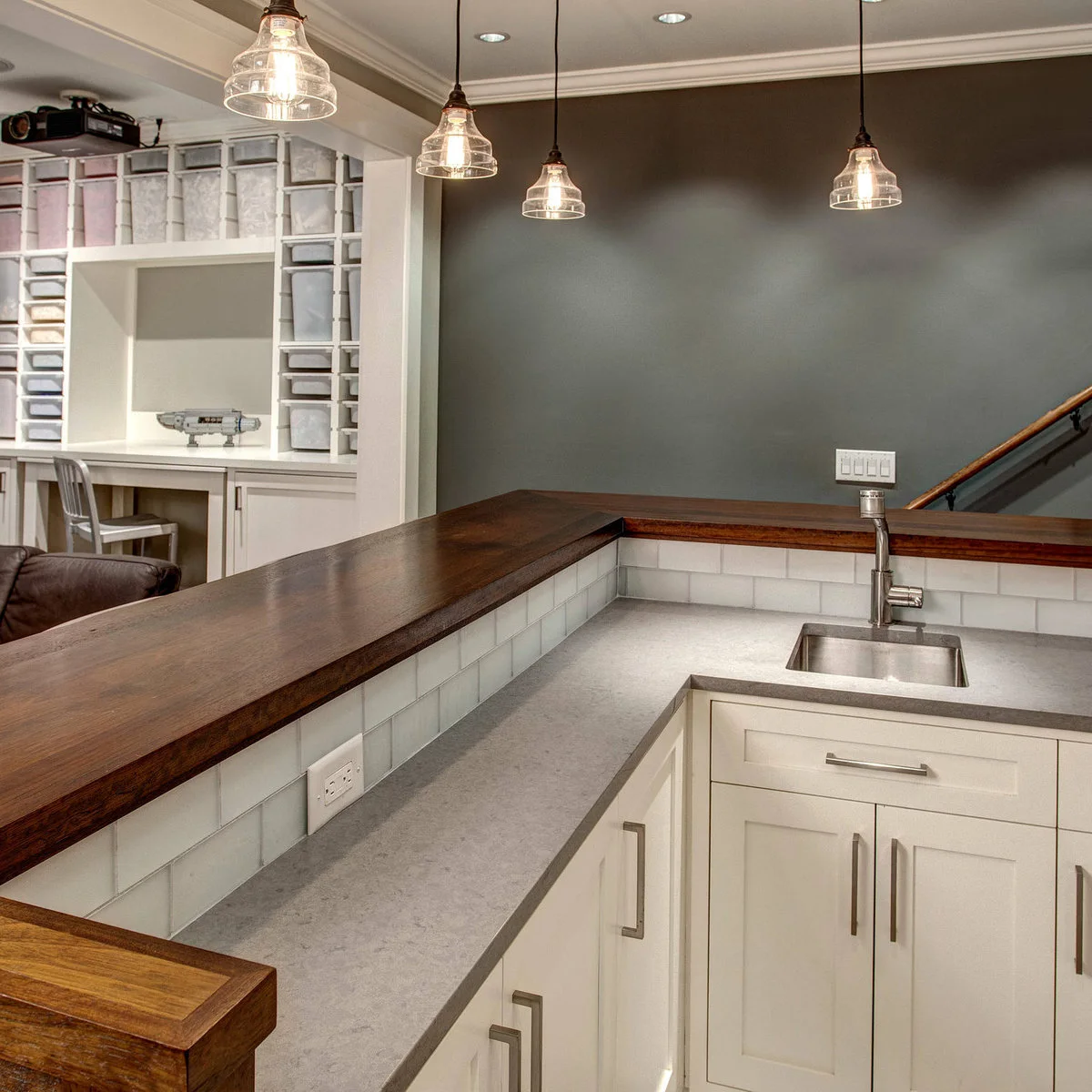 View inside a white basement bar with sink, continuous pale worktop and raised wood-colored edge