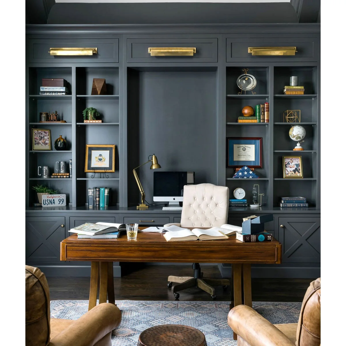 Wood writing table with cream chair in front of dark shelves and a separate computer counter