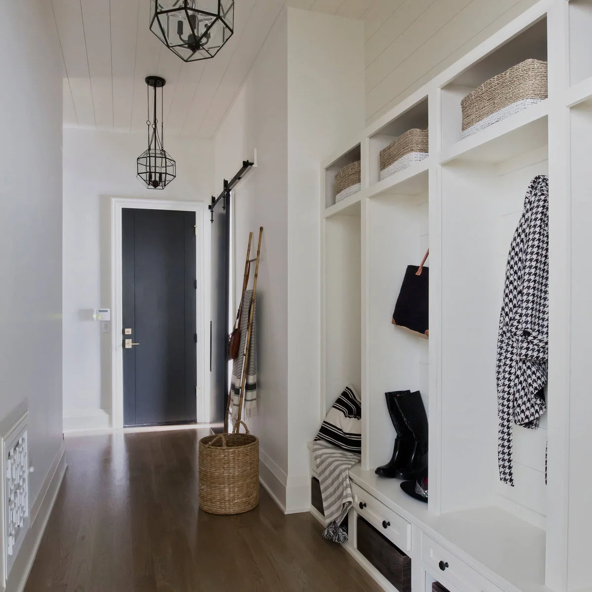 White entrance hall with a dark door, fitted bench, drawers, cubbies and baskets along one wall.