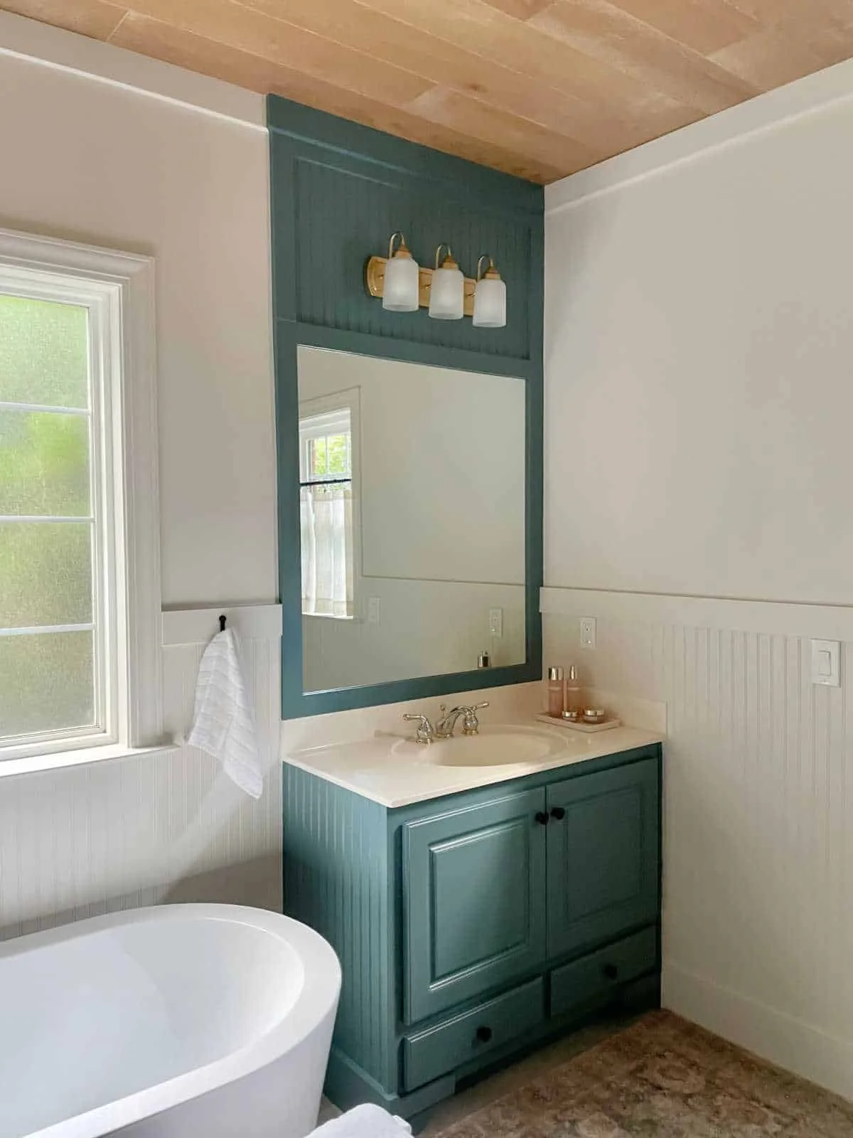 Blue-green vanity and matching large mirror frame with vertical panel detail above it and a three-light fitting.