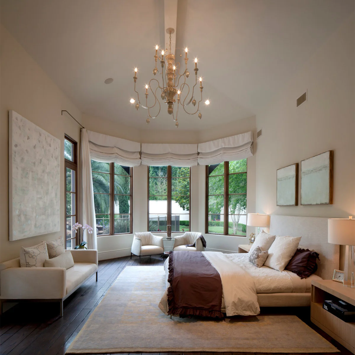 A large pale rug sits beneath a bed while a sofa and two chairs occupy the surrounding dark wood floor.
