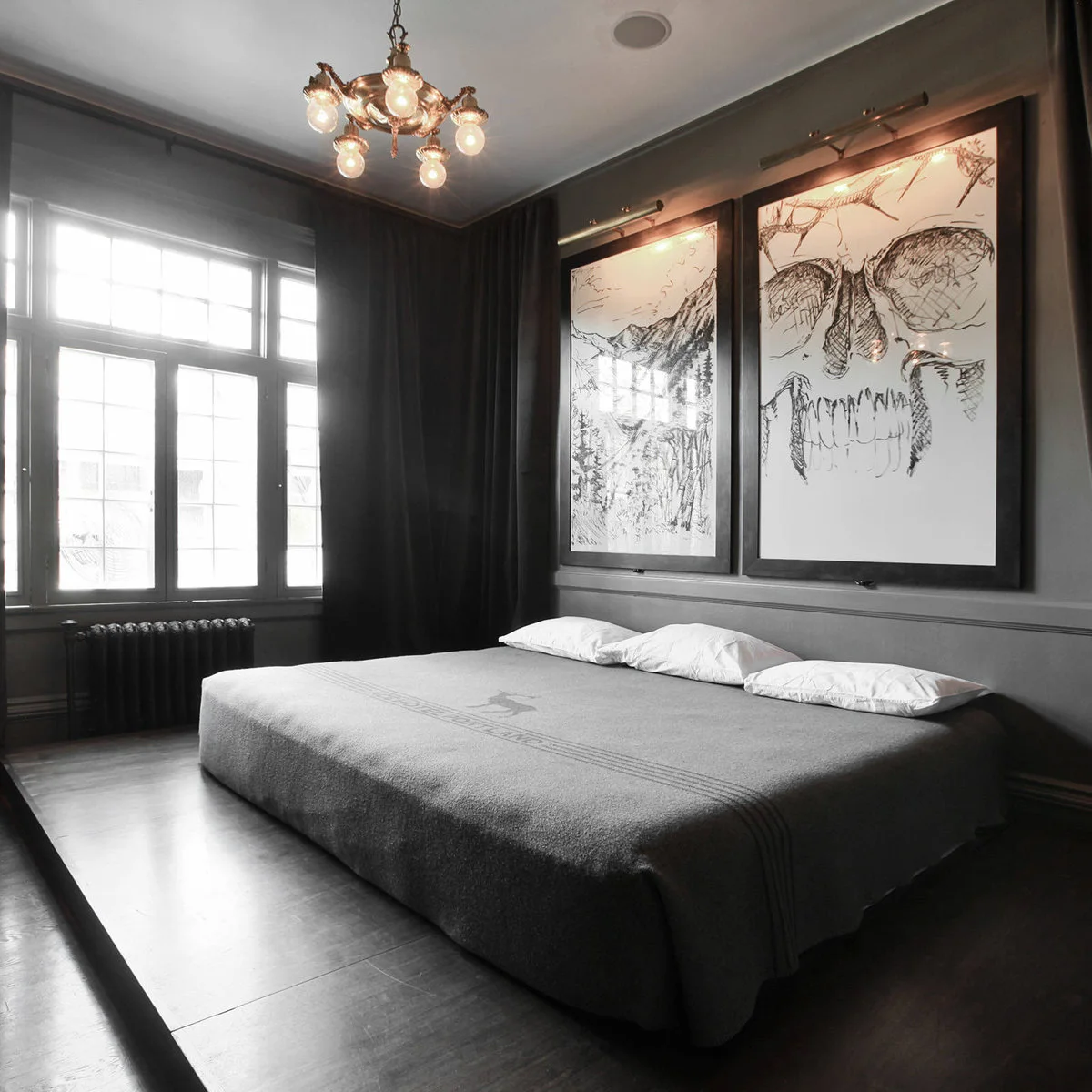 Dark grey bedroom with two large drawings above a low bed, picture lights and a tall window
