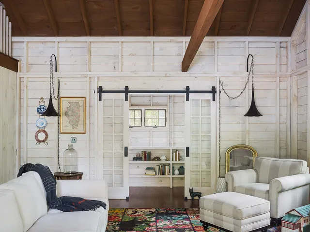 Pale upholstered seating sits beneath a timber ceiling beside a patterned rug and warm furniture.