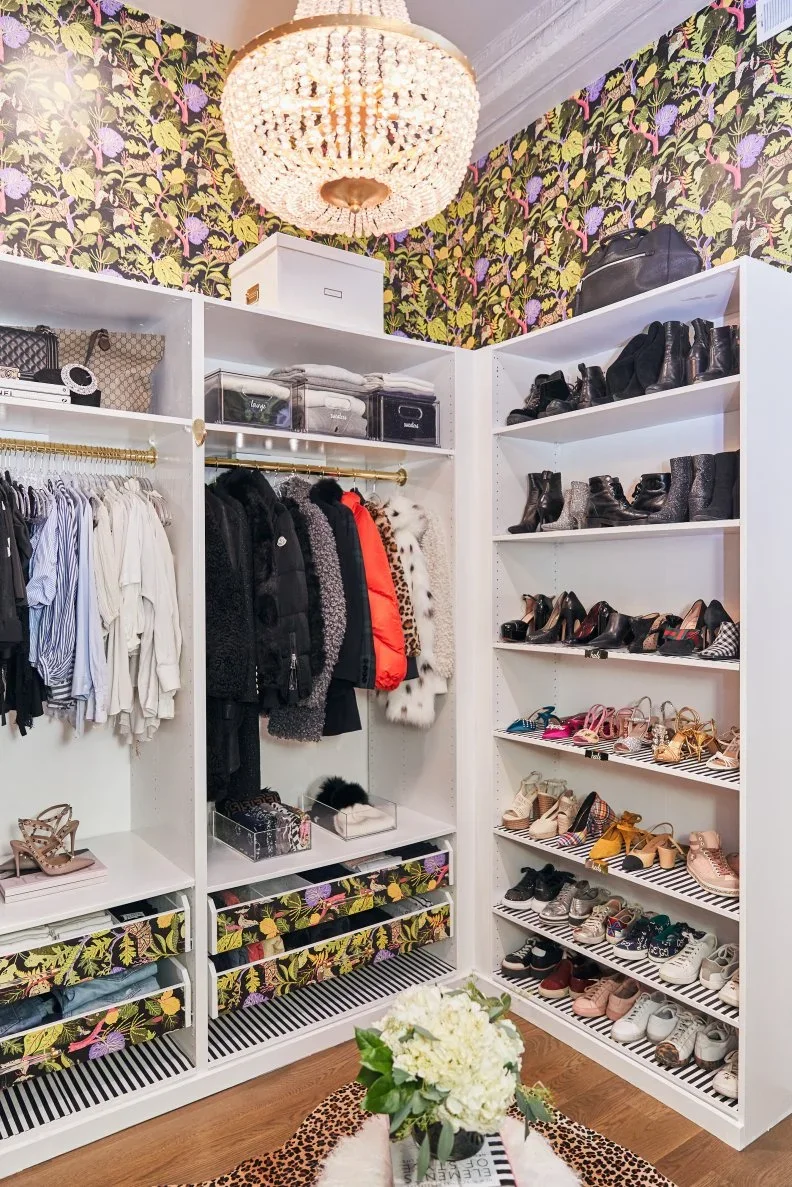 White open closet shelves and rails sit beneath botanical wallpaper, with matching patterned drawer fronts.
