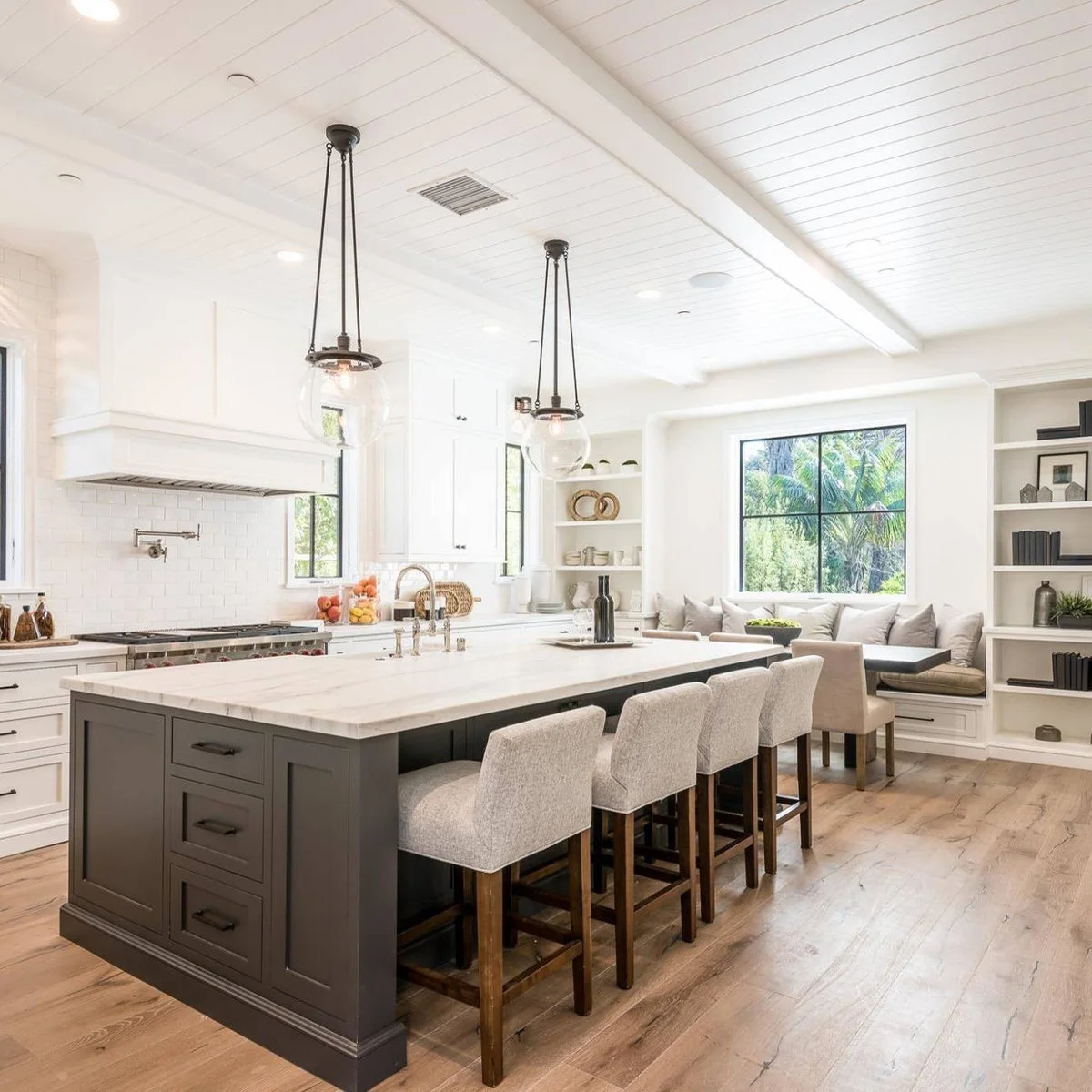 Long dark kitchen island with end drawers beside a window banquette and small table