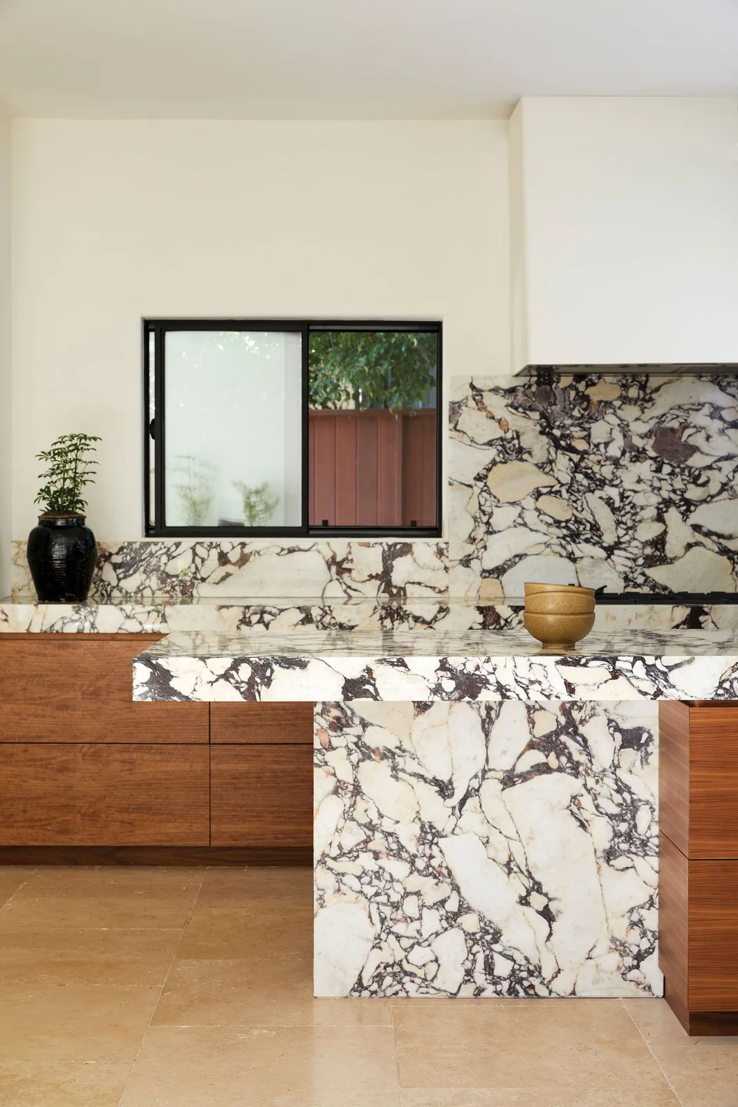 Flat walnut lower cupboards sit beneath boldly veined white and purple stone counters and backsplash around a waterfall island.