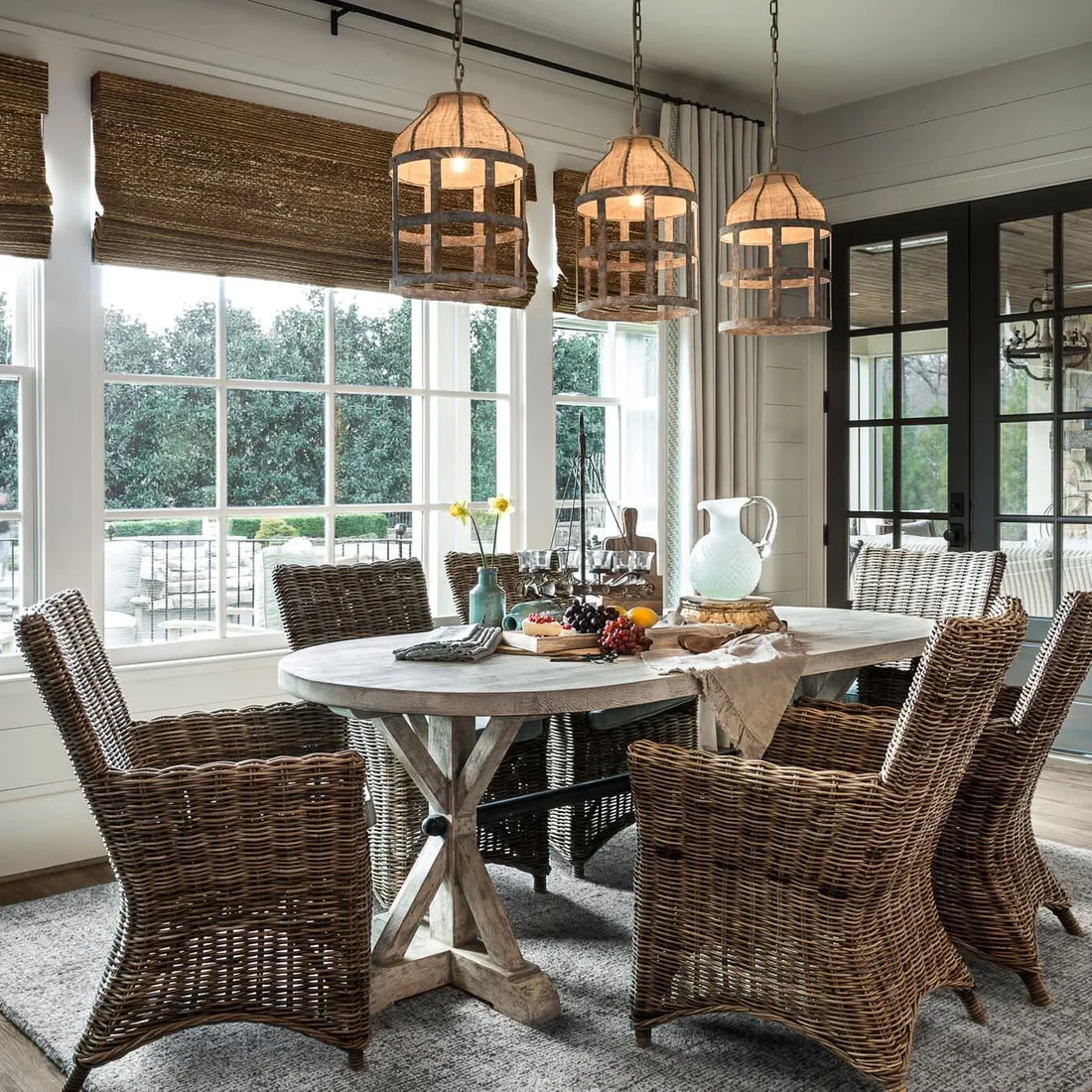 Pale wood oval dining table with cross supports, woven armchairs and three woven pendants near windows