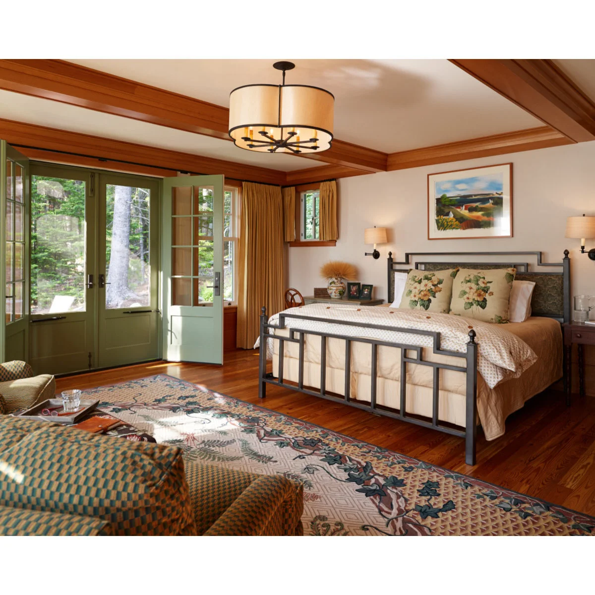 Bedroom with brown ceiling beams and window trim, green doors and a tan bed cover beneath floral pillows.