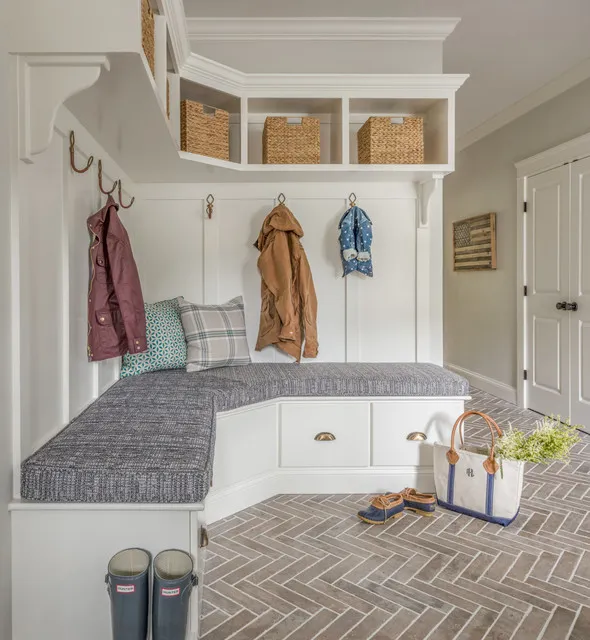 A white corner bench sits below coat hooks and open cubbies with woven baskets.