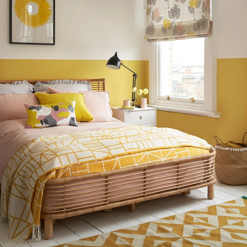 A yellow lower wall meets white above a bed with pink bedding, a yellow patterned throw and a black adjustable lamp.