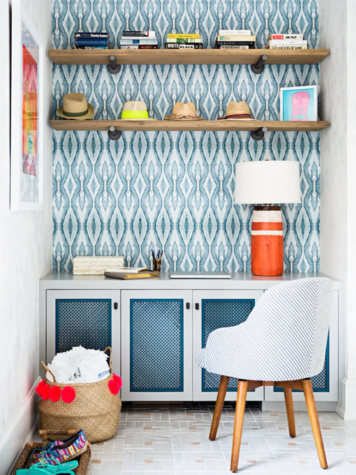 A low gray cabinet with blue mesh door panels sits below wood shelves holding hats and books, against blue patterned wallpaper.