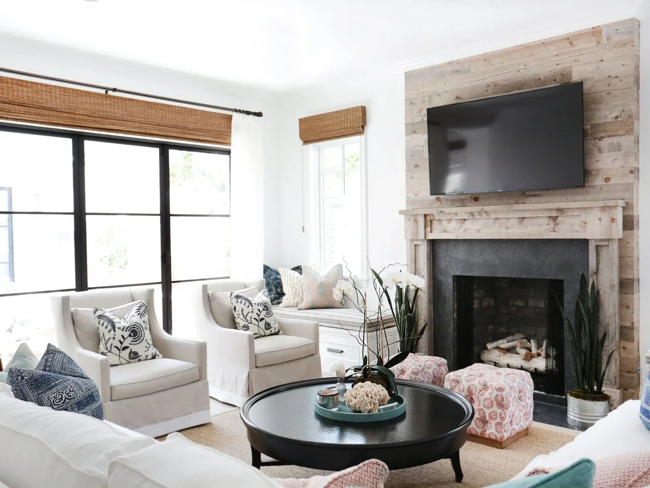 Weathered timber cladding surrounds a dark fireplace border beneath a television in a pale sitting room.