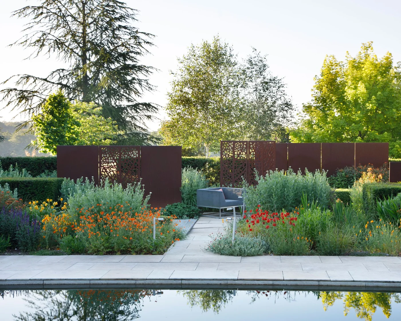 Solid reddish panels and patterned metal sections surround gray seating among flowering beds